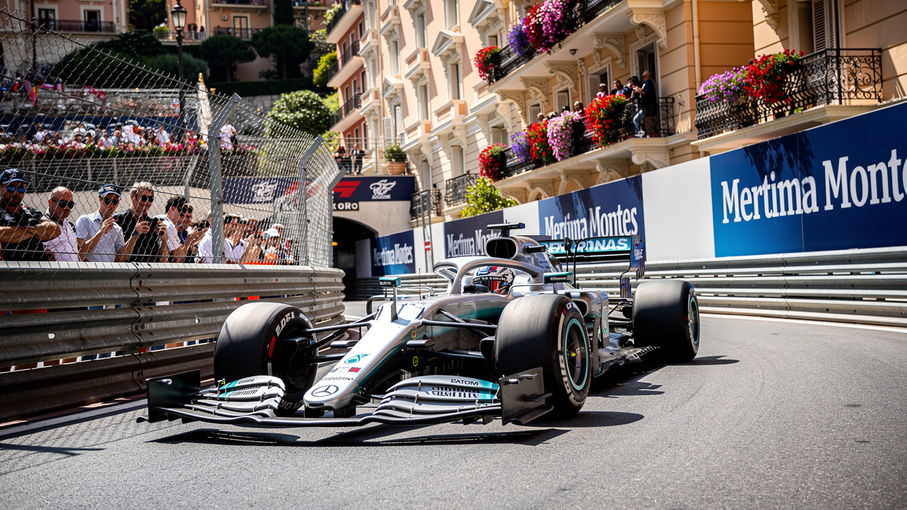 Silver Mercedes F1 car racing through Monaco street circuit corner